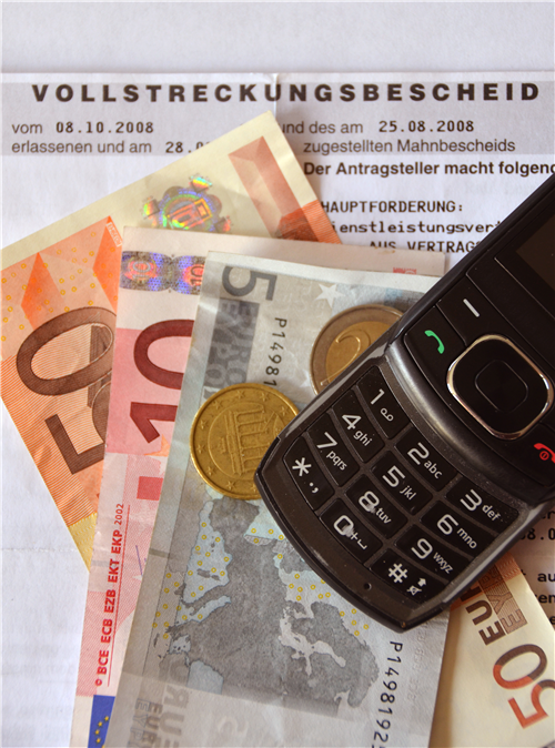 Auf einem Volstreckungsbescheid liegt etwas Geld und ein Handy
