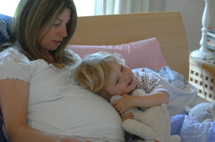 Eine sitzende, schwangere Frau mit einem Kleinkind das seinen Kopf auf dem Bauch liegen hat 