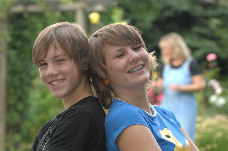 Zwei Jungendliche stehen Rücken an Rücken und lachen in die Kamera